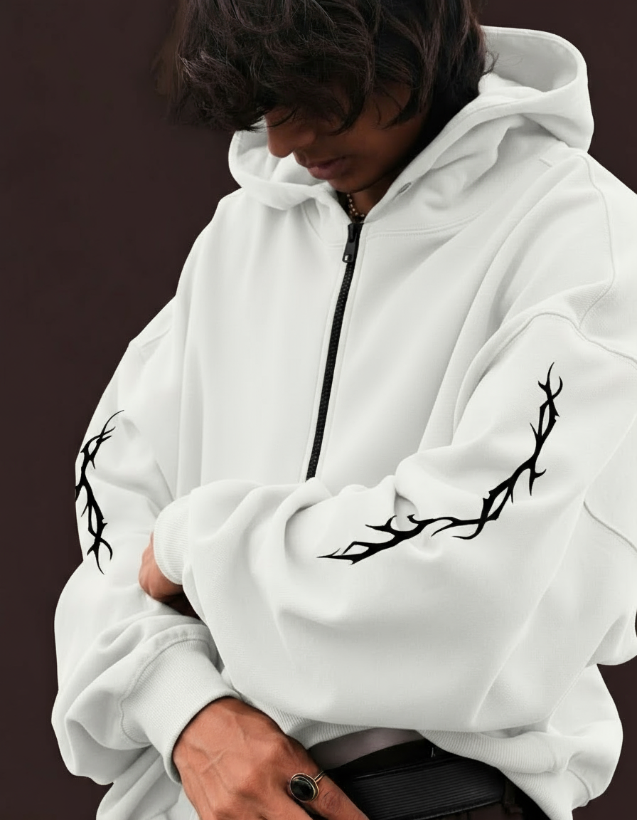 Person wearing a white hoodie with black tribal designs on the sleeves against a dark background
